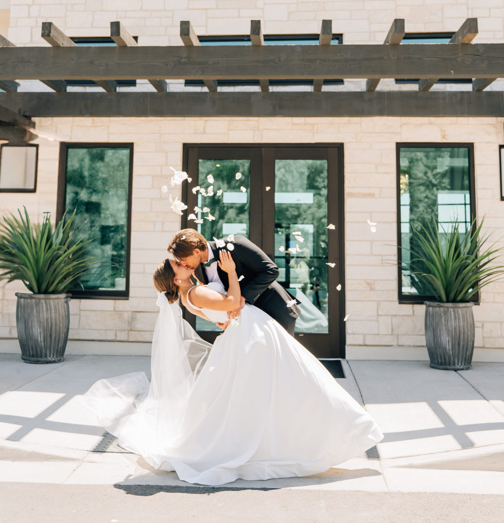 For a closer, candid moment: "A stylish couple sharing a kiss in front of the sleek, contemporary entrance of The OZ wedding venue in Utah during a sunset session."